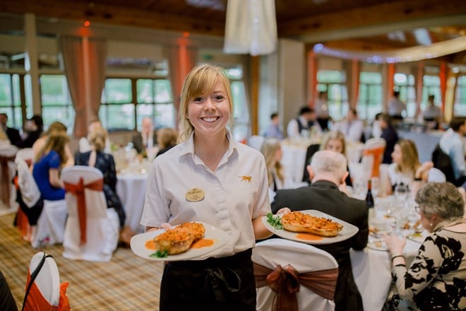 Woburn Safari Park catering employee holds two dishes in busy event room 
