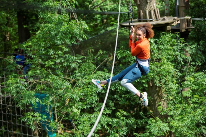 Young woman screams happily as she ziplines down high ropes course 